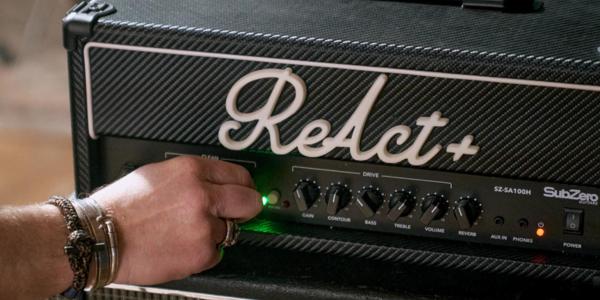 A hand turning the volume control on an amplifier that says ReAct+